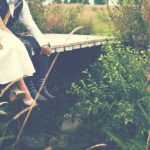 Photographie d'un couple marié assis sur un ponton, à côté de grandes herbes.