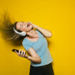 Photographie d'une jeune femme qui chante avec un casque sur les oreilles et son téléphone dans la main.