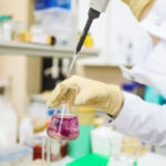 Photographie d'un chimiste en laboratoire, qui pipette une solution rose dans un erlenmeyer.