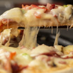 Photographie d'une pizza , une part coupée montrant le fromage fondu.