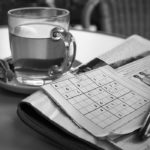 Photographie d'une tasse de thé, à côté d'un journal et d'une page de sudoku.