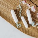 Plateau en bois portant des fleurs de coton ainsi que trois tampons hygiéniques.